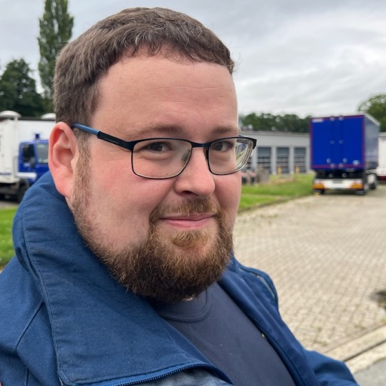 Johannes Rudolph in blauer Einsatzkleidung auf einem Unterkunftshof, im Hintergrund Fahrzeuge und Anhänger